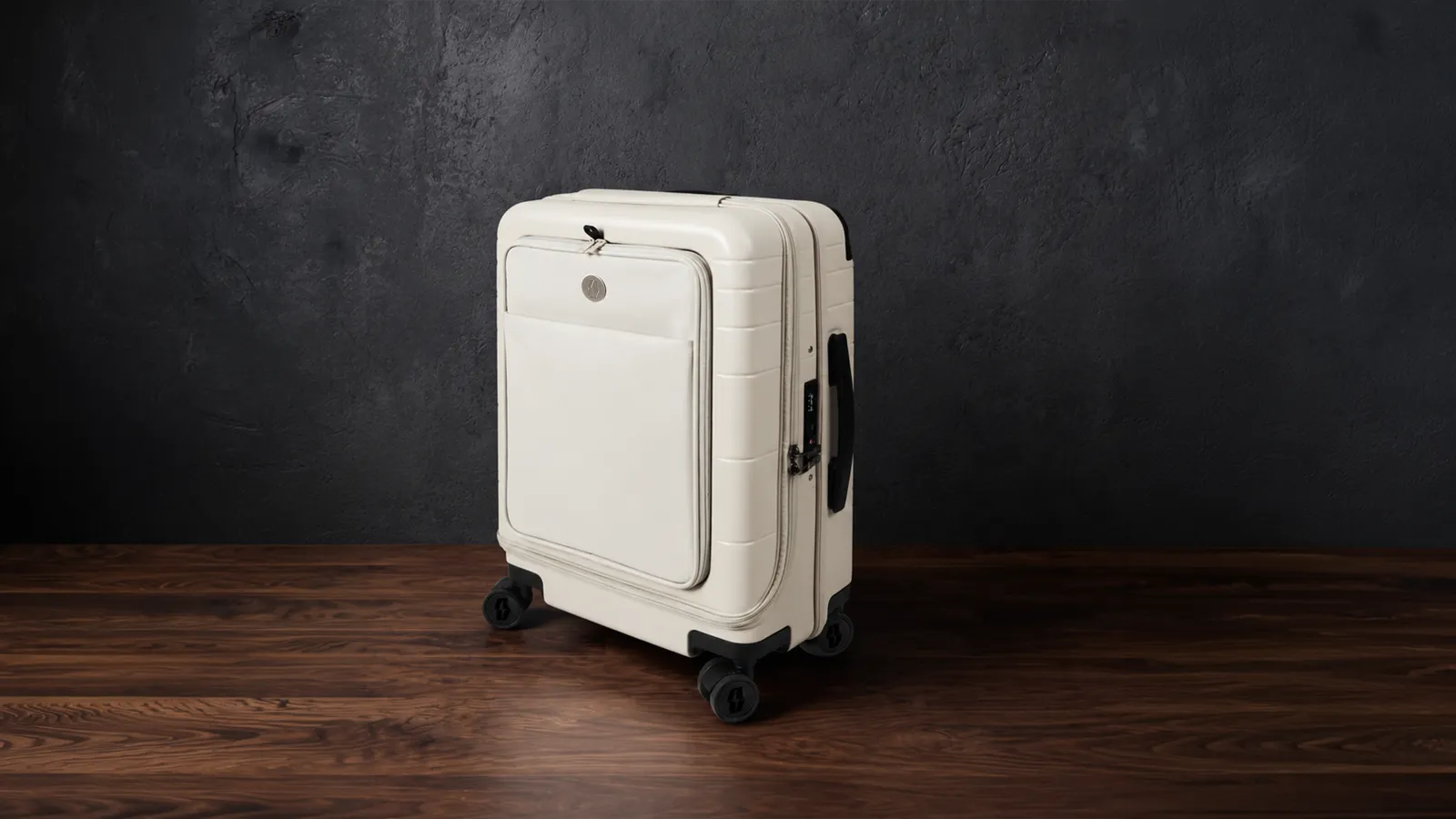 The cream Vasy carry-on standing in a dark studio, warm light across the shell.
