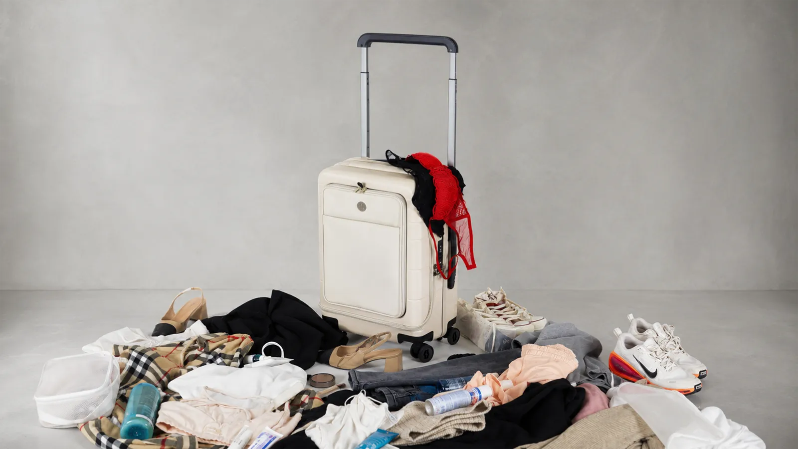 The Vasy carry-on standing composed beside a chaotic pile of clothes and travel gear it replaces.